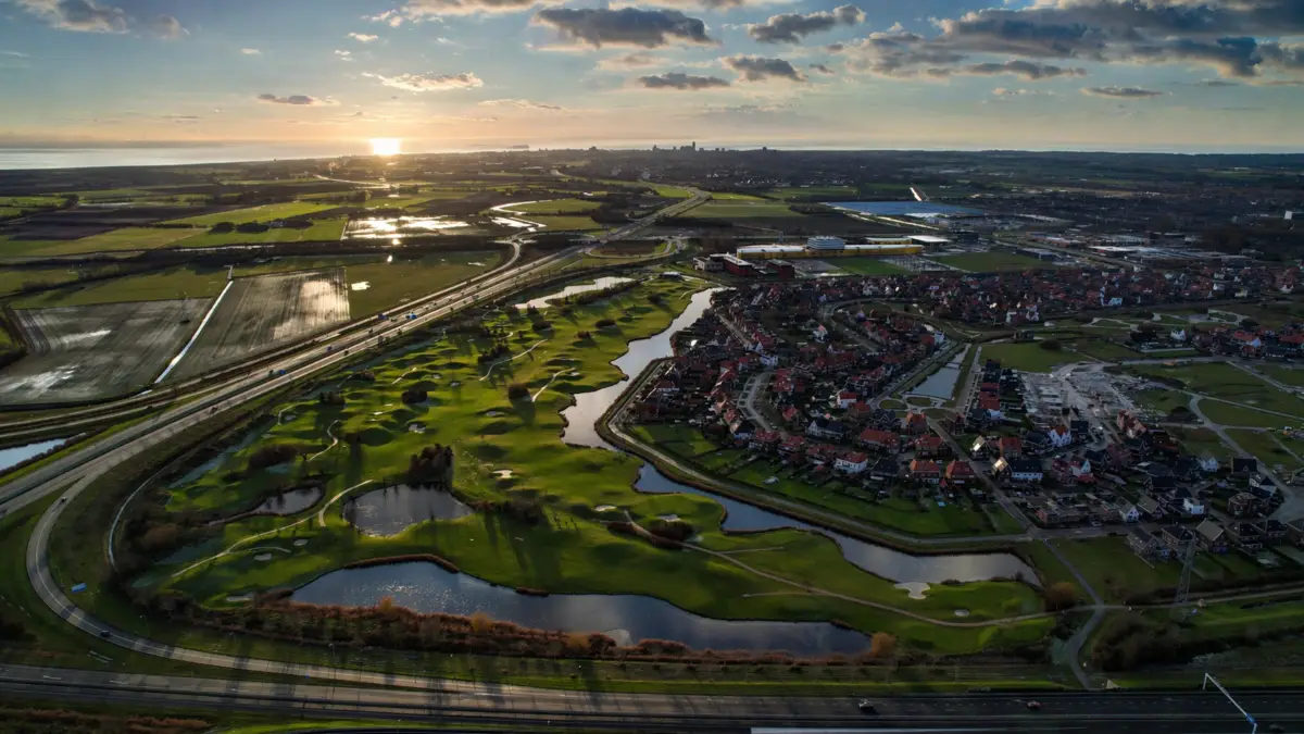 Drone luchtfoto van golfbaan en woonwijk bij zonsondergang in Nederland